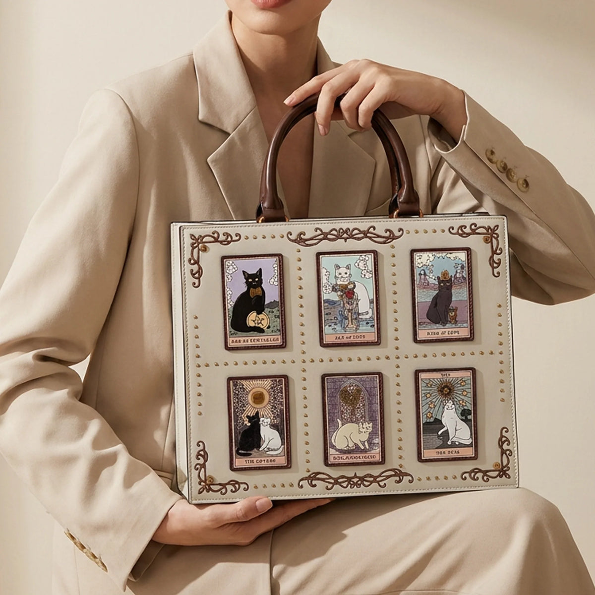 Three luxury handbags in brown and beige tones with gold hardware, styled on pedestals with white flowers and a perfume bottle against a beige backdrop with draped curtains.